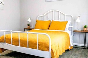 A bed with a white metal frame and a yellow bedspread. There are two bedside tables with lamps and small potted plants.