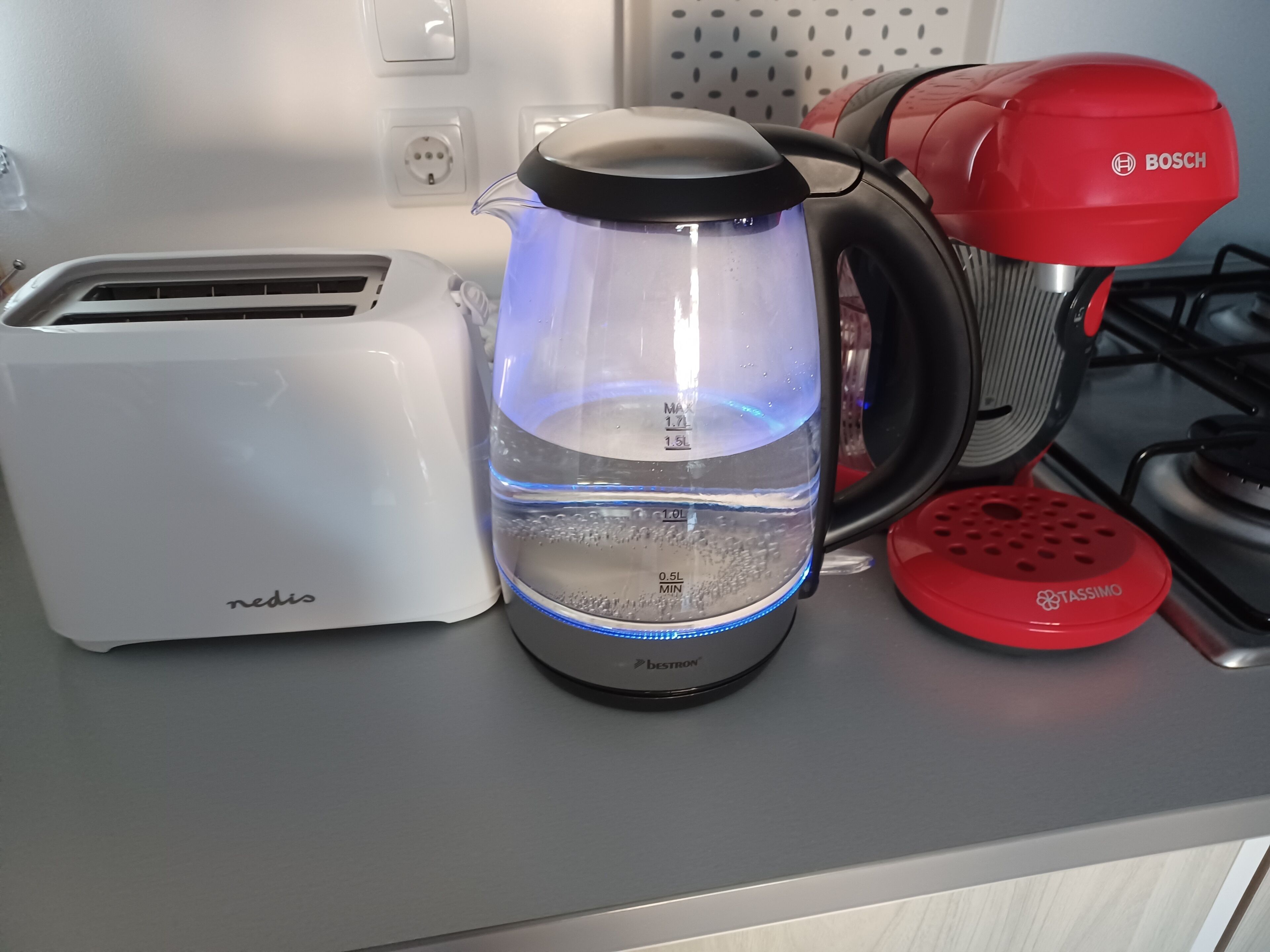 A kitchen with a water kettle, a toaster, and a red electric kettle on the counter.