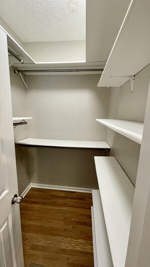 Functional walk-in closet with a minimalist design, featuring a door, shelves, and a light fixture.