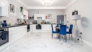 A modern kitchen with white cabinetry, a marble countertop, and a dining area with blue chairs.