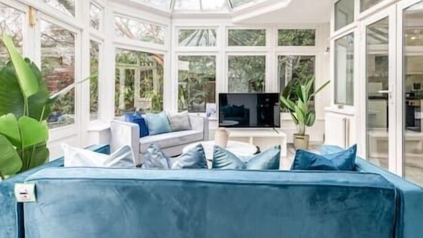 A conservatory with a blue sofa, a television, and large windows.