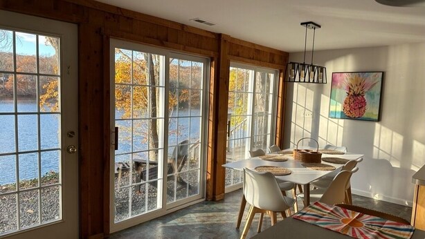 A dining area with a table set for four, large windows with a view of a lake, and a wooden interior. - Lakefront Connecticut Oasis - Updates throughout  (Oxford)