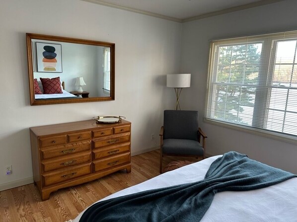 A bedroom with a bed, a dresser, a chair, a lamp, and a window with blinds.