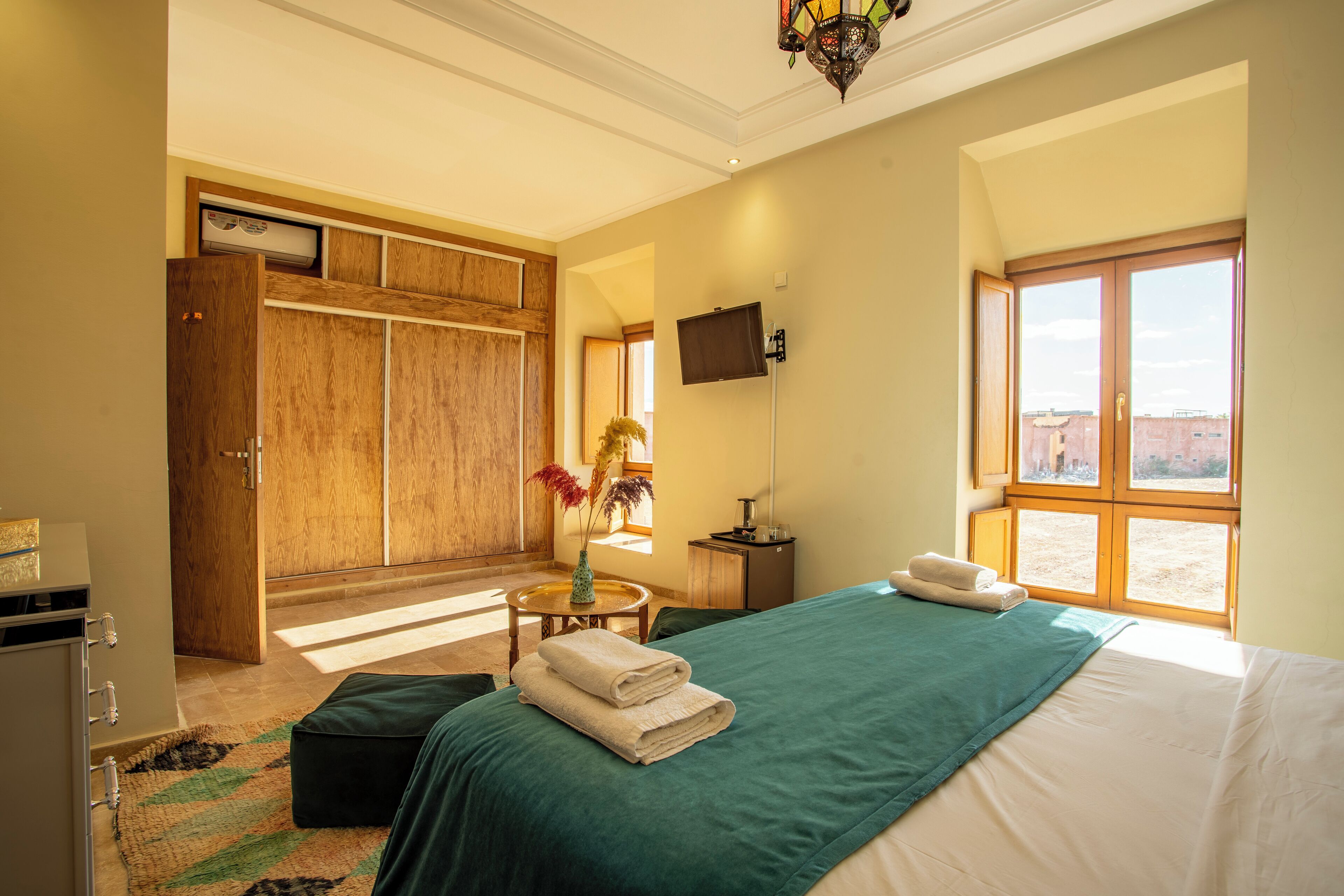 Habitación de hotel con una cama grande, un armario de madera, una mesita con un florero y un televisor en la pared.