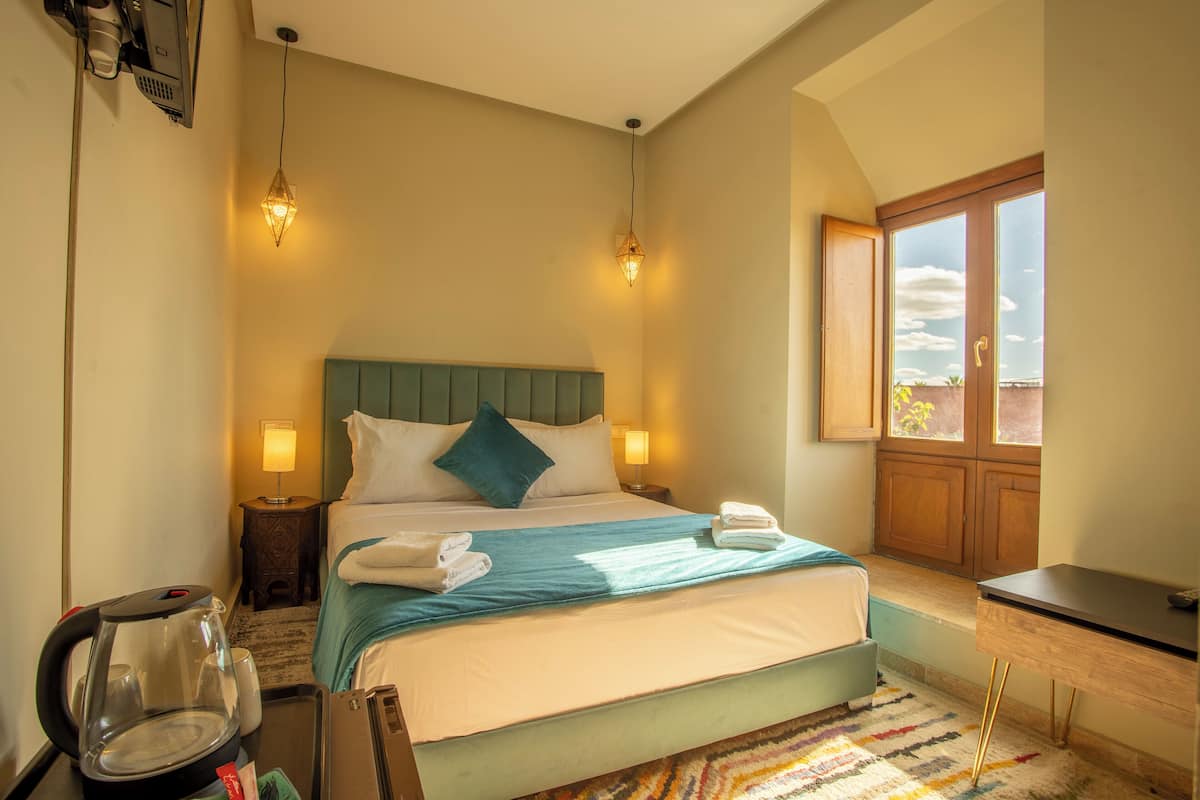 A hotel room with a bed, bedside lamps, a desk, and a window with a view.