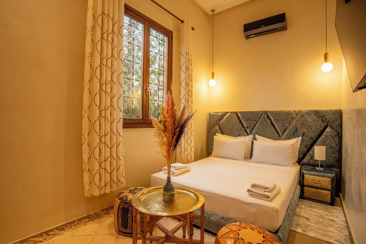 A neatly arranged bedroom with a bed, bedside table, and a small round table with a vase.