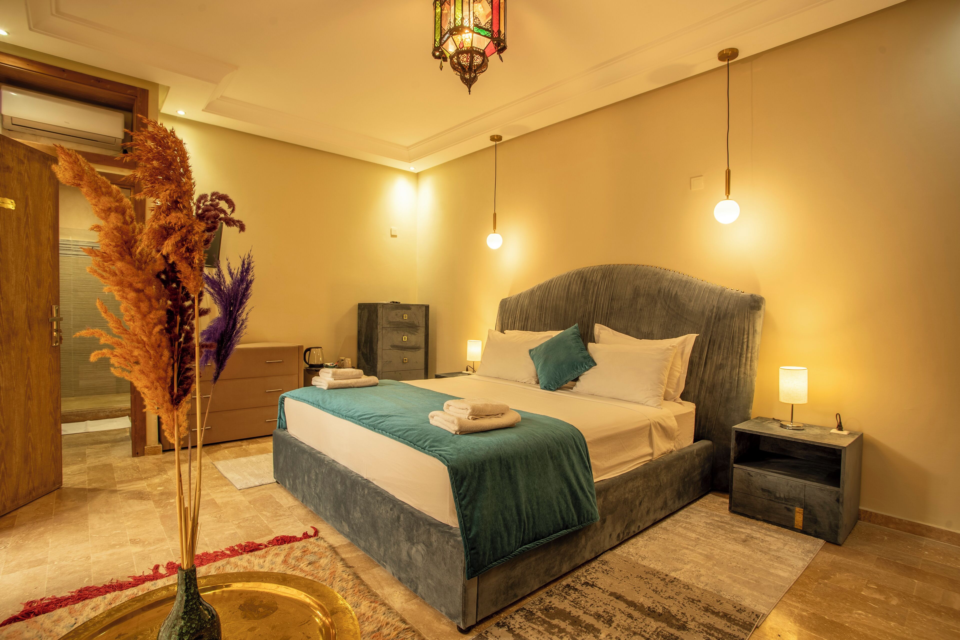 Un dormitorio moderno con una cama grande, mesitas de noche, una mesilla auxiliar y un jarrón decorativo con plantas secas.