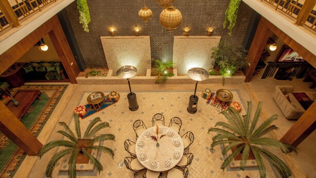 A spacious lobby with a central round table surrounded by chairs, a high ceiling with hanging lanterns, and a patterned floor.