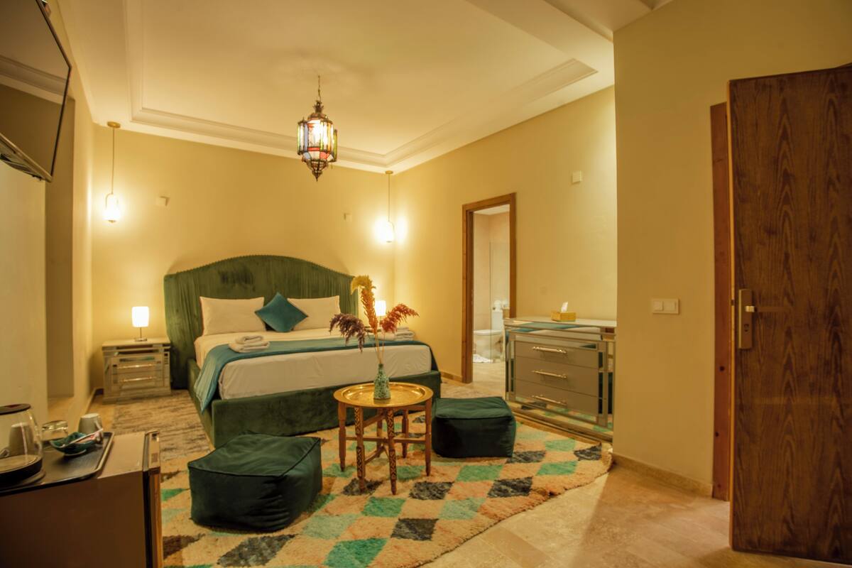 A hotel room with a bed, bedside tables, a mirror, a wooden door, and a small round table with a vase.