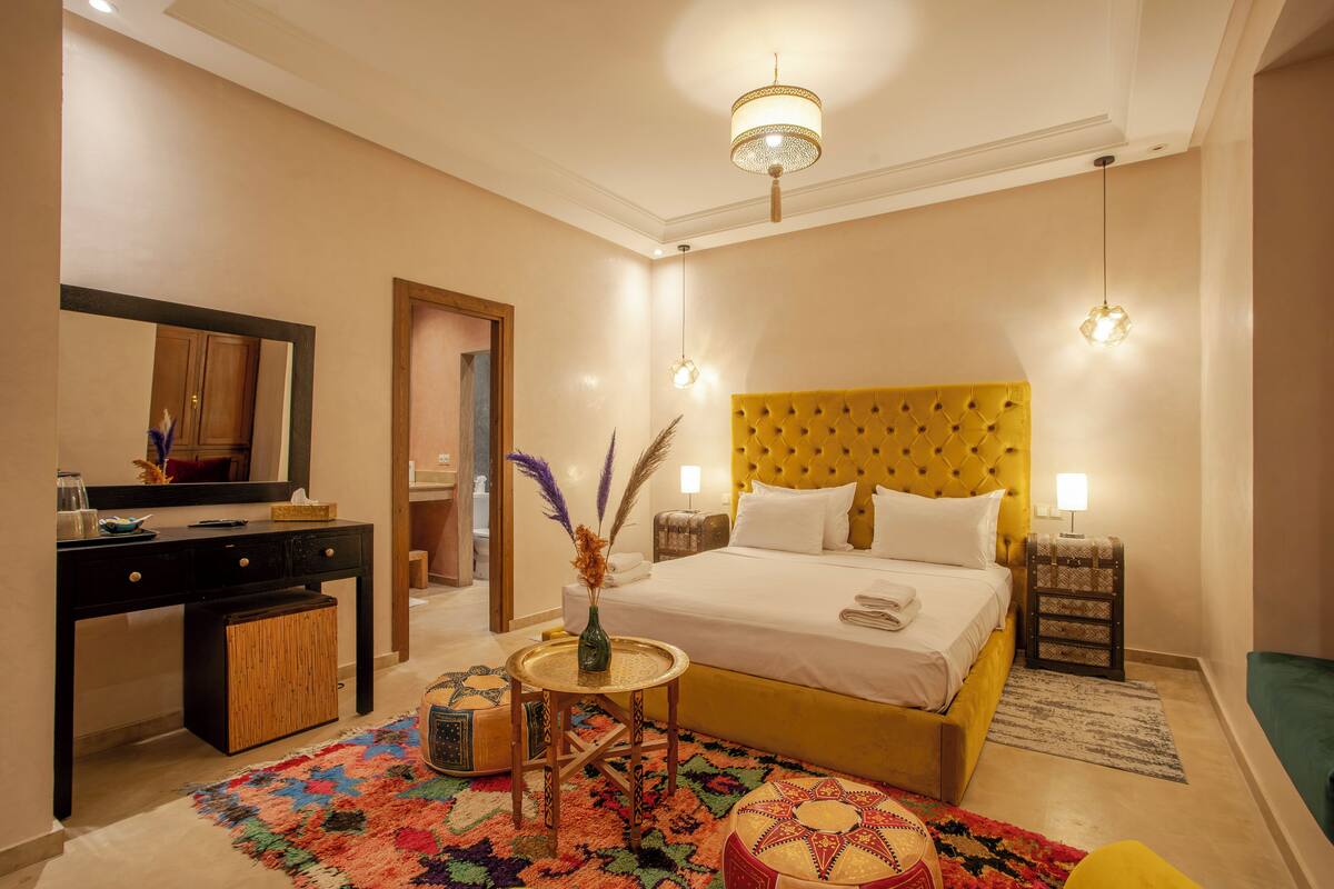 A hotel room with a bed, bedside table, lamp, and a desk with a mirror.
