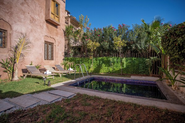 A pool area with lounge chairs, a small pool, and lush greenery.
