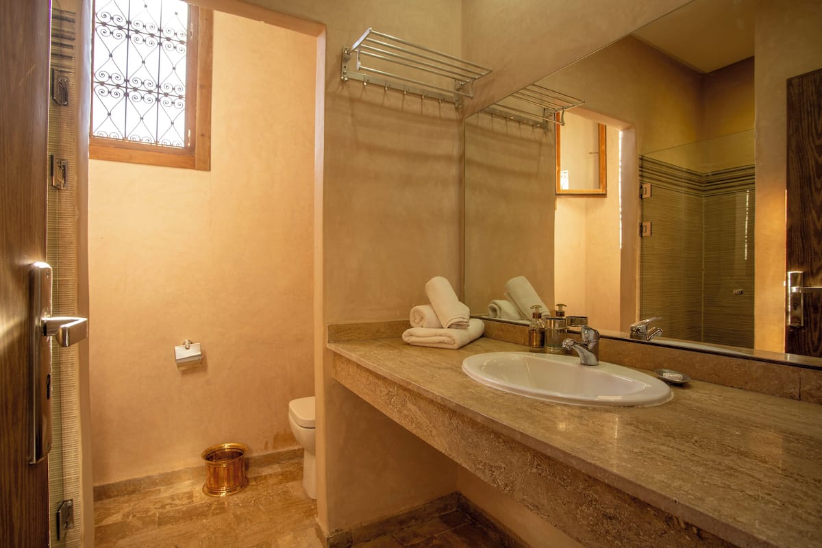 A bathroom with a sink, mirror, towel rack, and a window with a decorative grille.