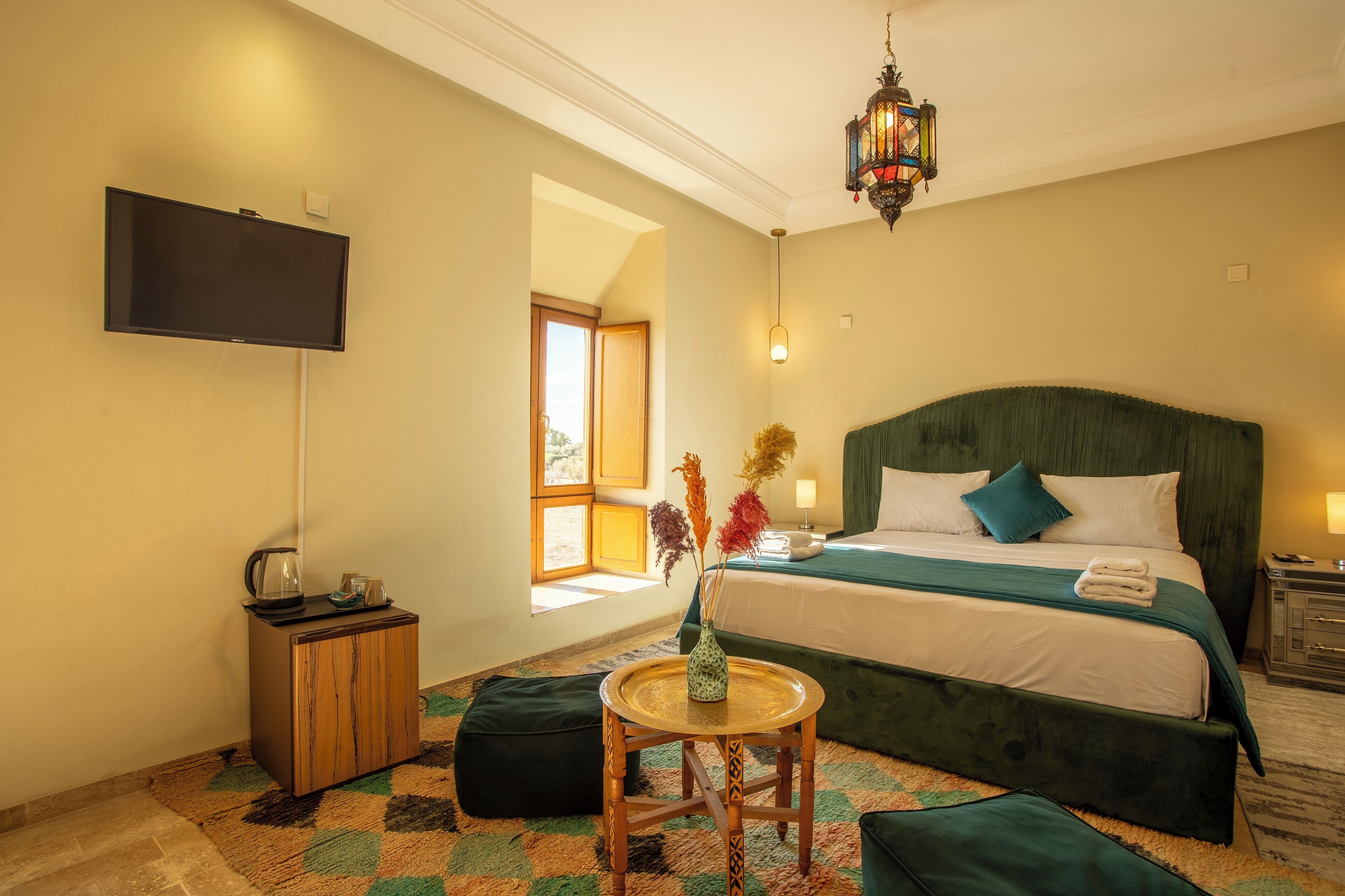 Habitación de hotel con cama, televisión, una mesita con un jarrón y ventana con vistas.