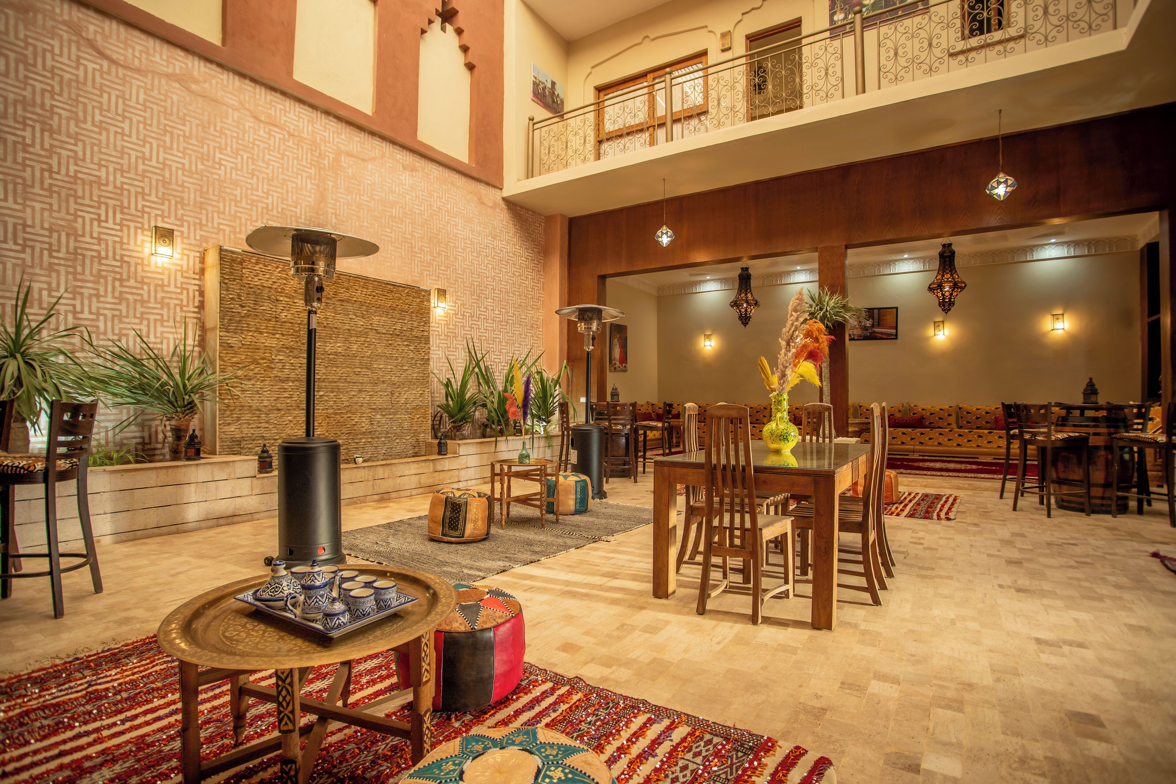 A spacious lobby with a high ceiling, a balcony, and a dining area with wooden furniture and a decorative centerpiece.