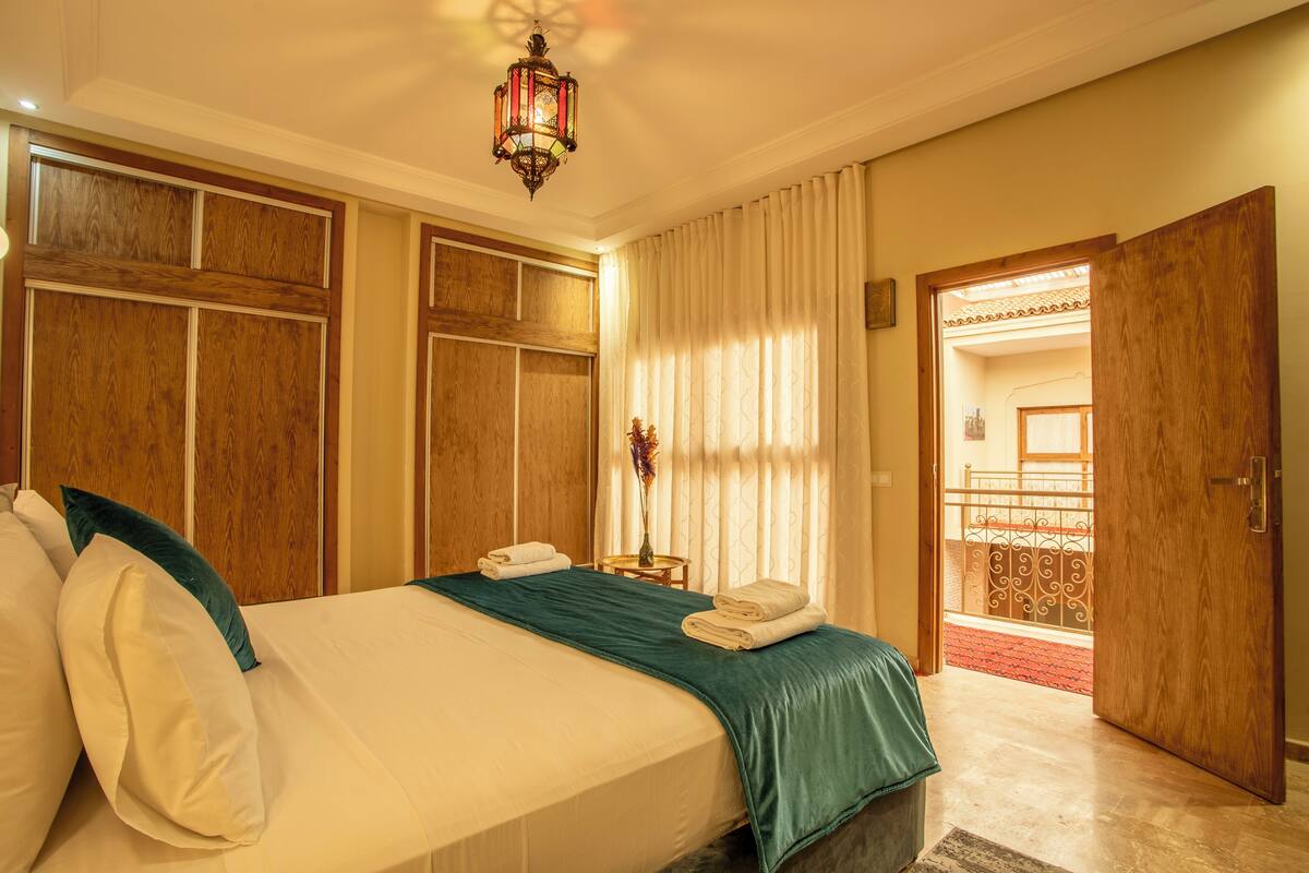 A hotel room with a large bed, wooden paneling, a green throw blanket, and a decorative lantern.