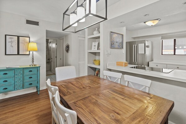 A dining area with a wooden table and white chairs, a turquoise cabinet with drawers, and a white countertop with a sink.