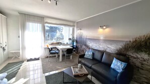 Een moderne woonkamer met een eethoek, een bank met kussens, een salontafel en een uitzicht op de natuur door een groot raam.