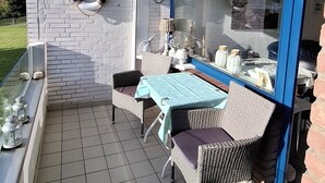 Een balkon met een tafel en stoelen, een bakstenen muur, een raam met luiken en een reddingsboei.