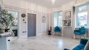 Een ruime woonkamer met een marmeren vloer, een grijze deur, een klein zwart tafeltje en twee blauwe fauteuils.