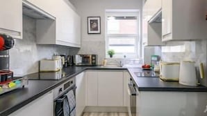 Een smalle keuken met witte kasten, een zwart aanrecht en een raam dat natuurlijk licht binnenlaat.