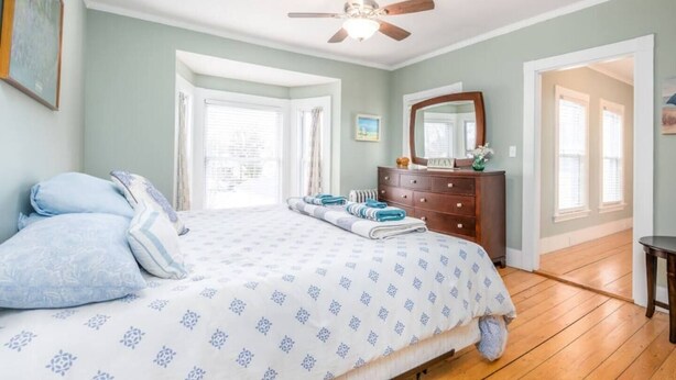 A bedroom with a bed, a dresser, a ceiling fan, and a door leading to another room.
