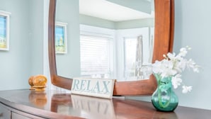 A wooden dresser with a mirror, a 'RELAX' sign, and a vase with flowers.