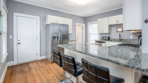 A modern kitchen with a granite countertop, stainless steel appliances, and bar stools.