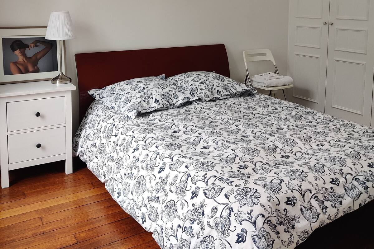 Un dormitorio con cama, mesita de noche, lámpara, silla y armario.