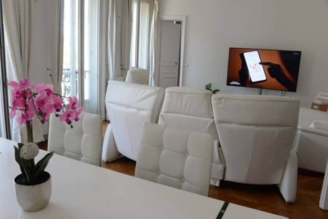 Un salón moderno con sofás de cuero blanco, un televisor de pantalla plana y una orquídea en maceta.