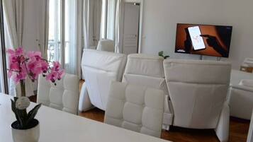 Un salón moderno con sofás de cuero blanco, un televisor de pantalla plana y una orquídea en maceta.