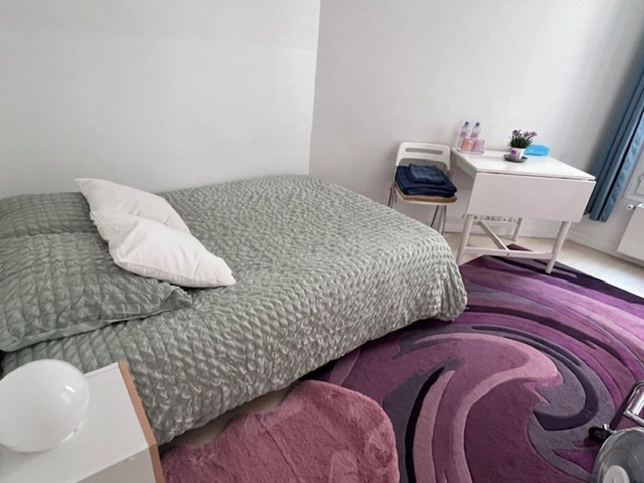 A bedroom with a bed, a bedside table, a chair, and a small desk with a chair.