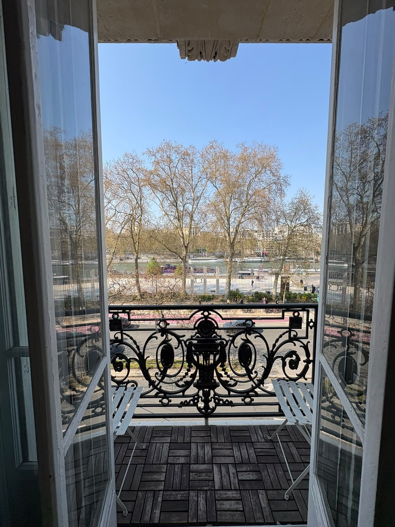 A balcony with a wrought iron railing, a view of leafless trees, and a distant building.