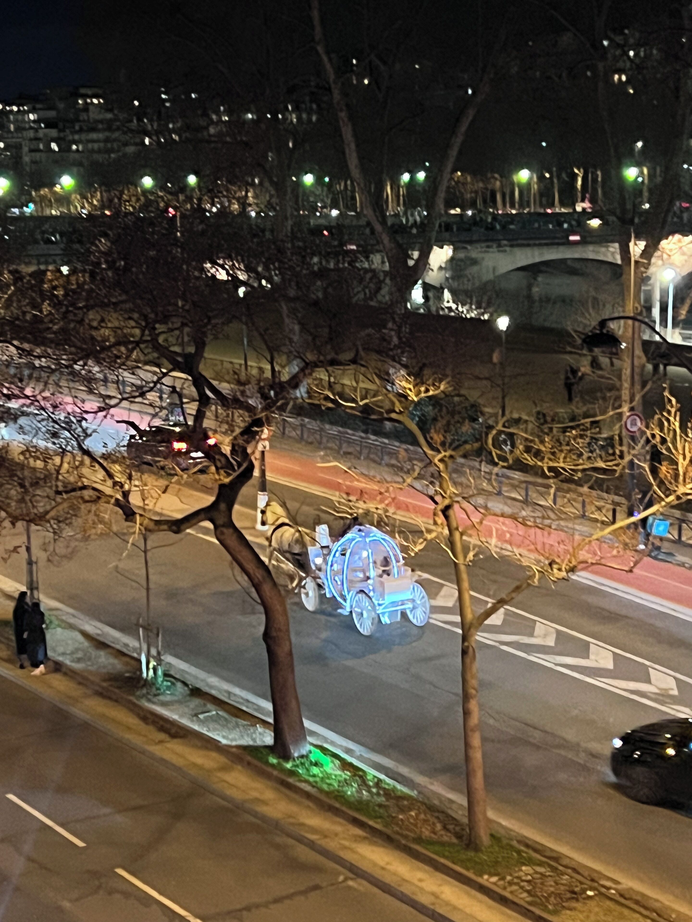 A nighttime street scene with a decorative illuminated carriage on the road.
