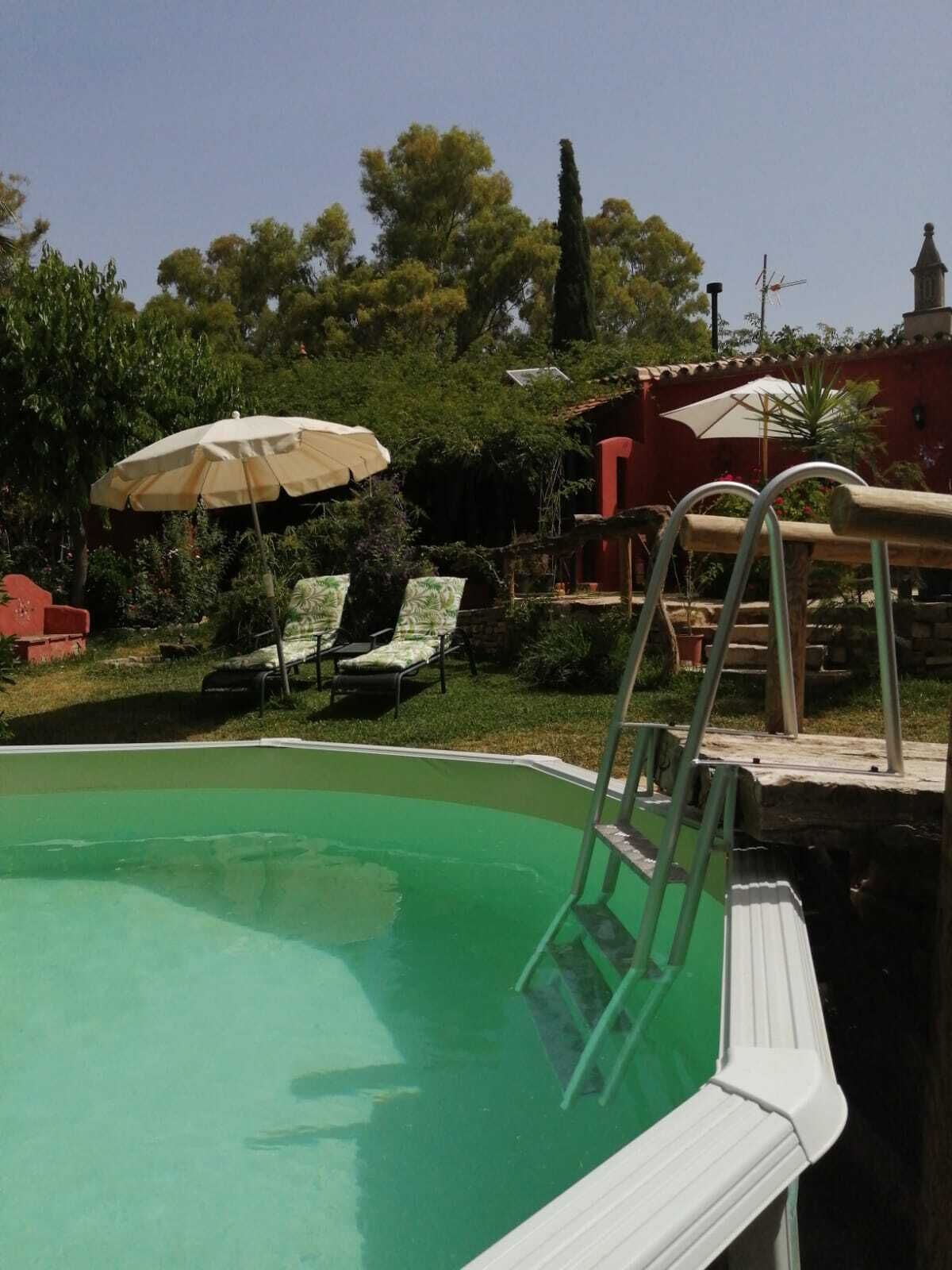 A swimming pool with a ladder, lounge chairs, and umbrellas.