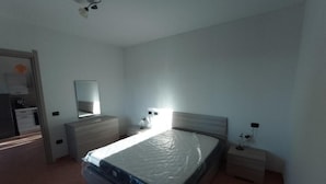 A bedroom with a bed, a dresser, a nightstand, a mirror, and a wall-mounted light fixture. - agriturismo tres montes (Sorso)