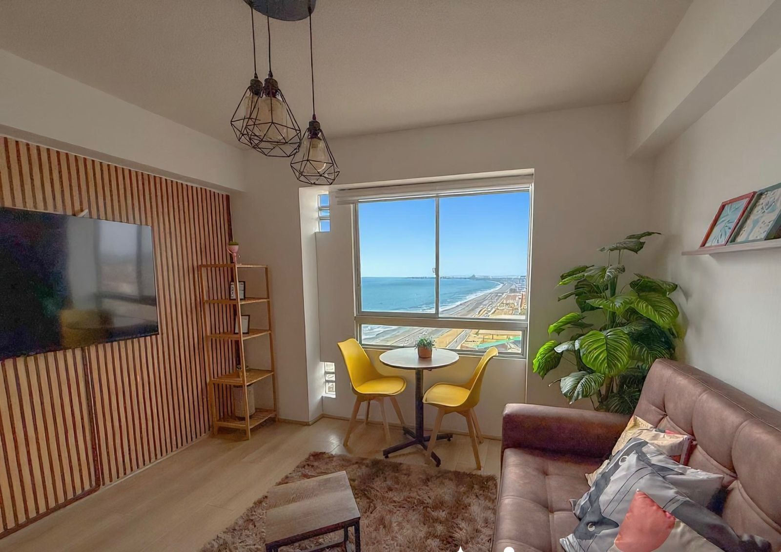 A living room with a large window, a TV, a sofa, a coffee table, and a bookshelf.