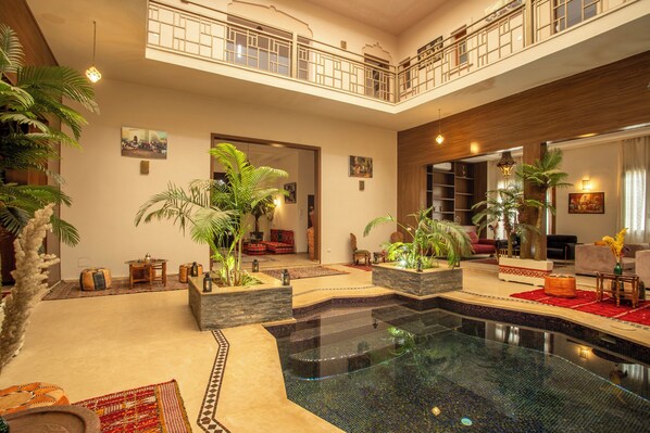 A spacious indoor pool area with a glass barrier, surrounded by seating areas and potted plants.