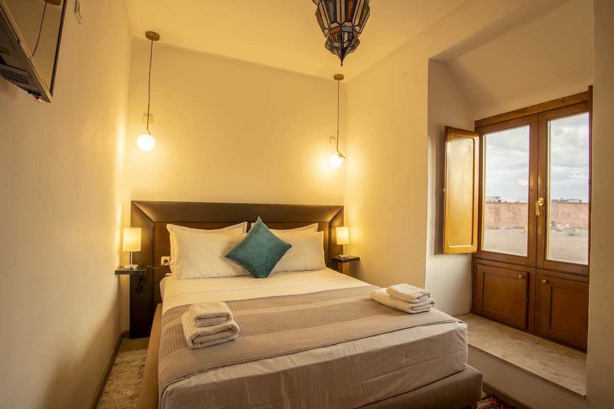 A hotel room with a large bed, two bedside lamps, a window with a view, and a ceiling light fixture.