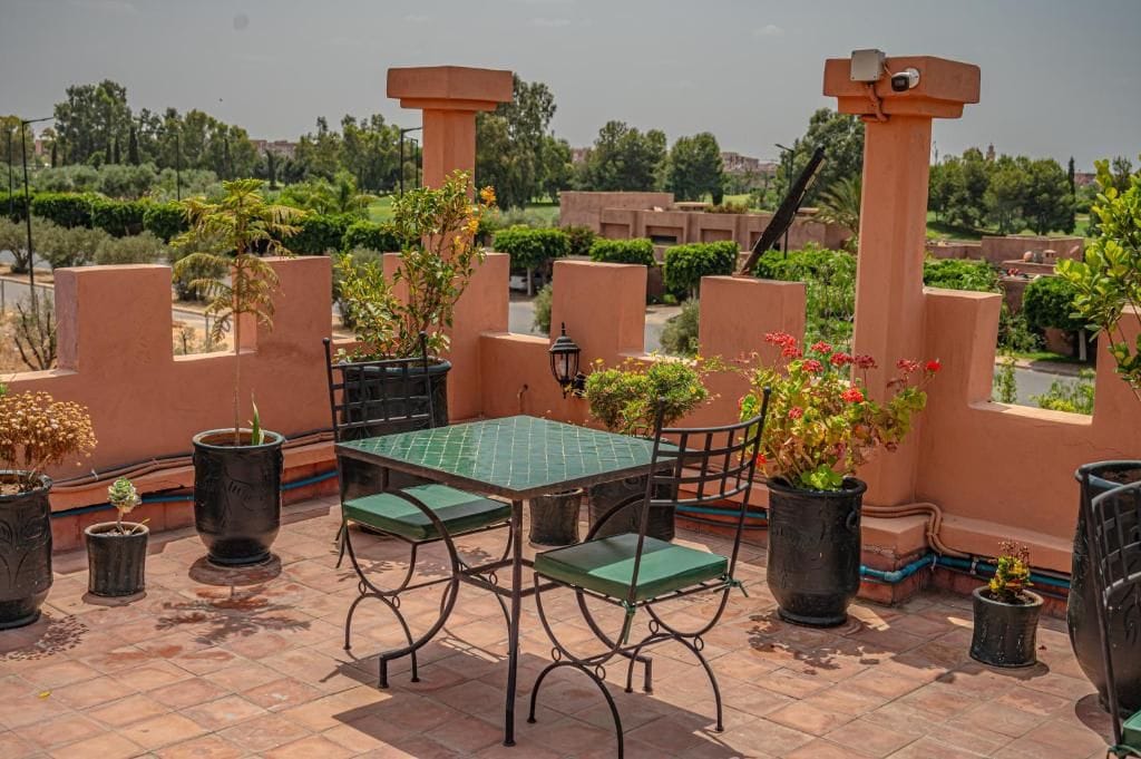 Une terrasse sur le toit, avec une table et des chaises, entourée de plantes en pot et offrant une vue sur le paysage urbain.