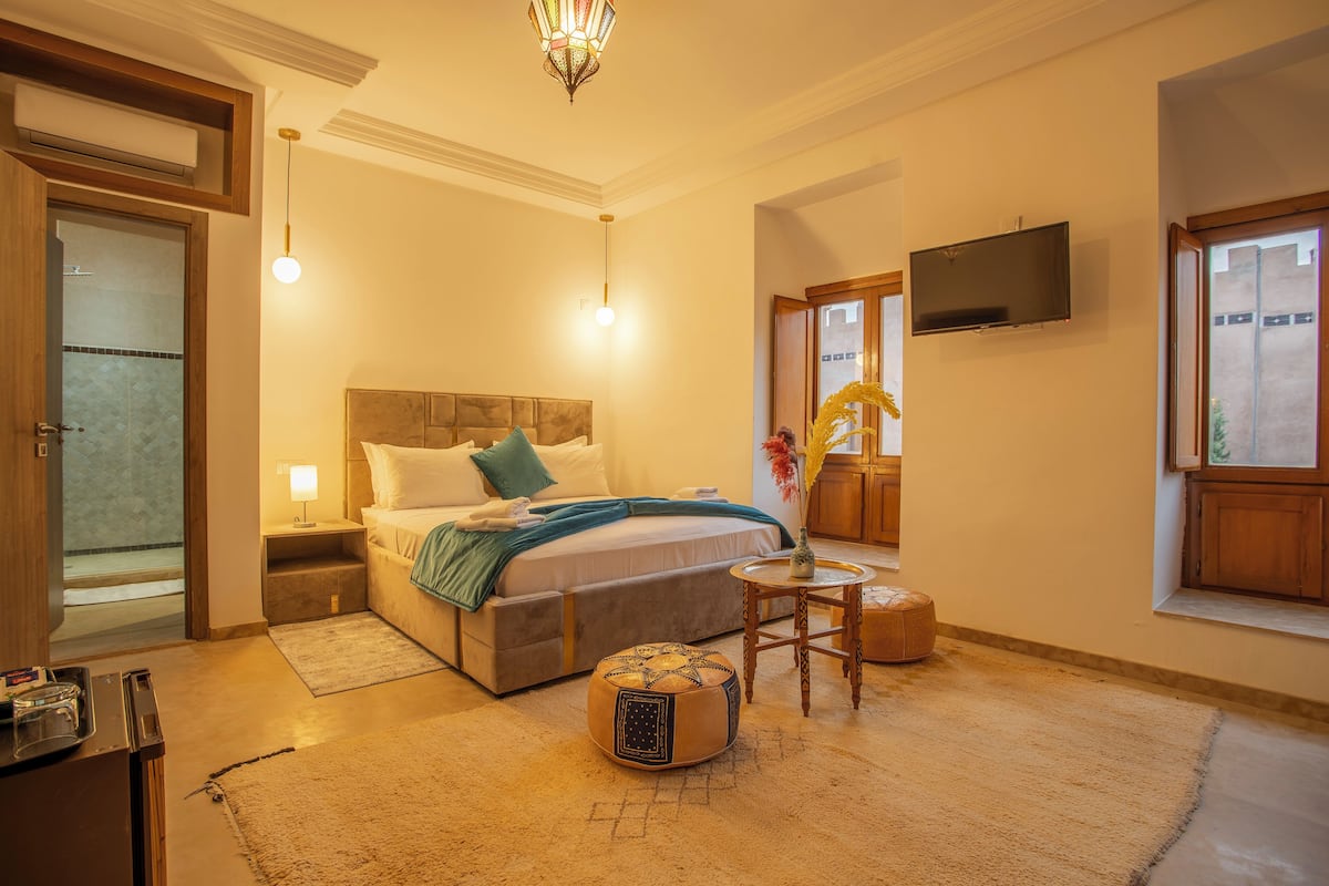 A bedroom with a bed, bedside table, lamp, and a small round table with a vase.