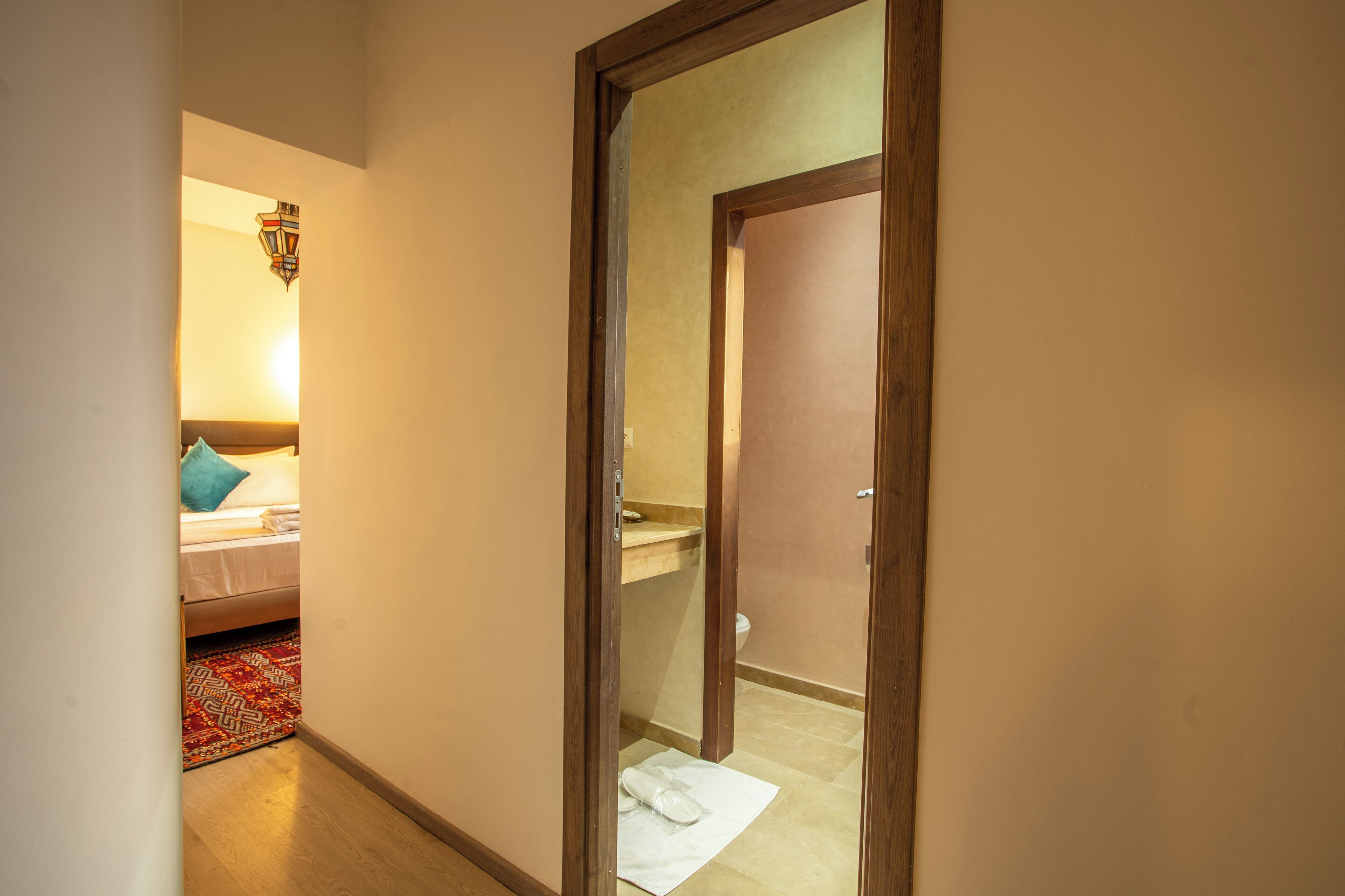 A narrow hallway leading to a bedroom with a bed, a bathroom with a sink, and a visible door frame.