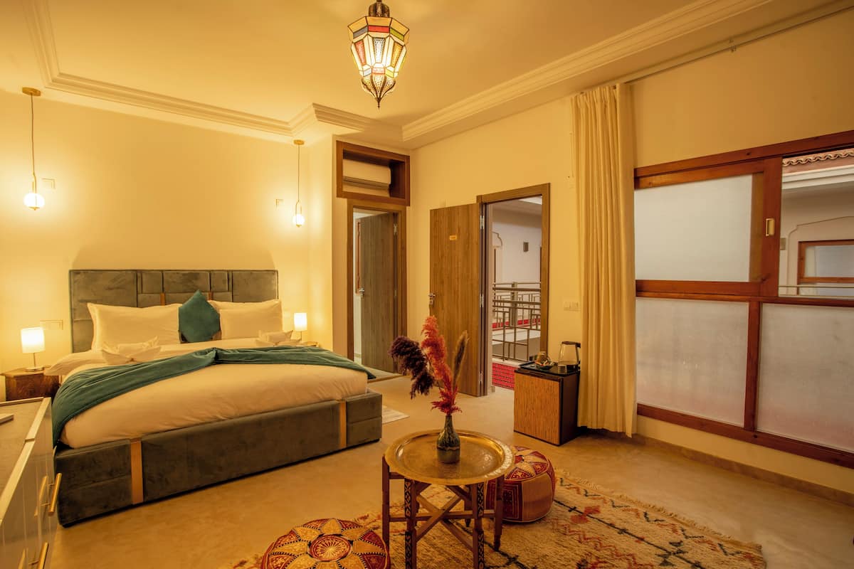 A hotel room with a bed, bedside table, lamp, decorative vase, and a view of the outside.