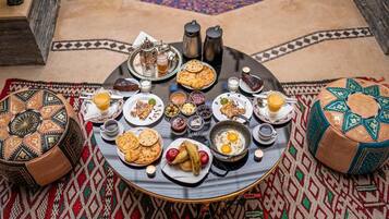 A round dining table with a variety of dishes, including bread, eggs, and fruits, set on a patterned rug.