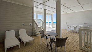 A covered outdoor area with white wicker furniture, a round table, and a staircase leading to a balcony with a view of the ocean. - Beach House - Anchors Aweigh by PHG (Panama City Beach)