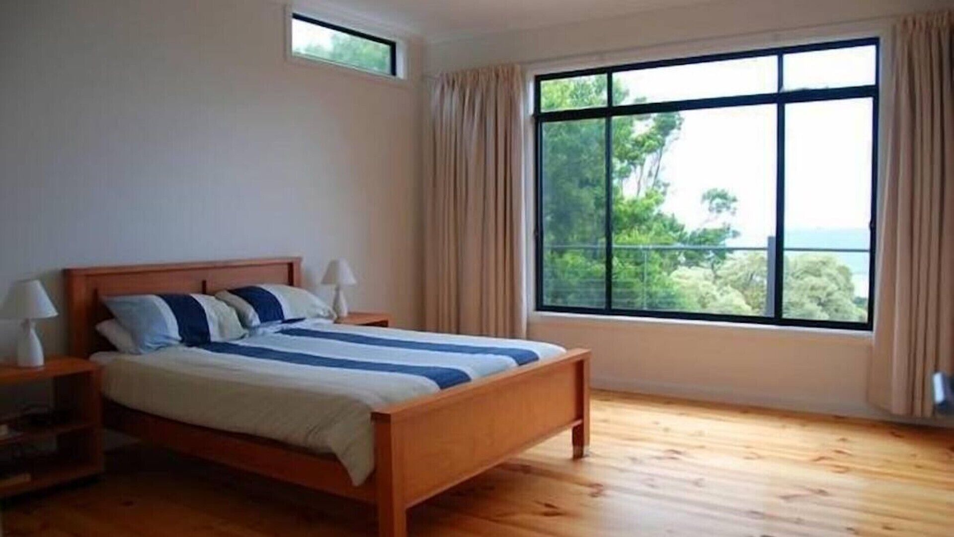 A bedroom with a wooden bed, a nightstand, a window with curtains, and a view of greenery outside.