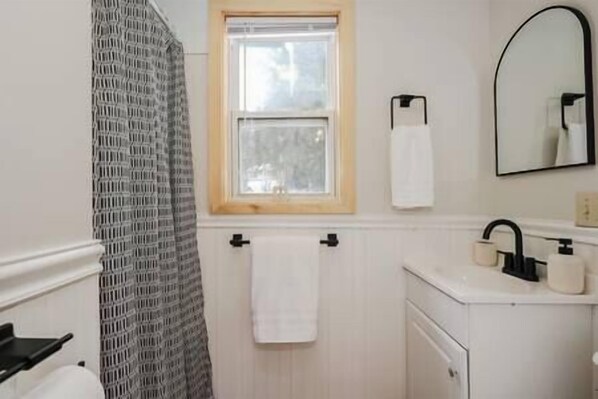Un baño con ventana, toallero, espejo y lavamanos.