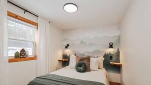 Ein Schlafzimmer mit einem Bett, einem Fenster, Wandgemälde und zwei Nachttischlampen.