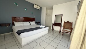 Ein ordentlich eingerichtetes Schlafzimmer mit einem großen Bett, einem Holzstuhl, einem kleinen Tisch und einer Klimaanlage an der Wand.