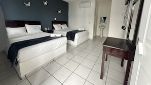 Ein Hotelzimmer mit zwei Betten, einem kleinen Tisch, einem Fernseher und einem Badezimmer mit Waschbecken und Spiegel.
