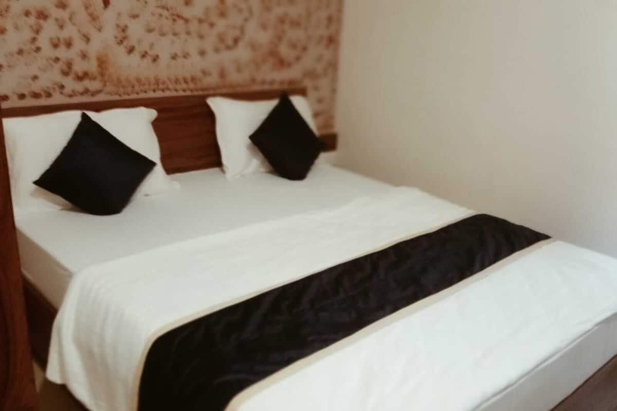 A neatly made bed with white bedding and black pillows, a wooden headboard, and a black throw blanket.